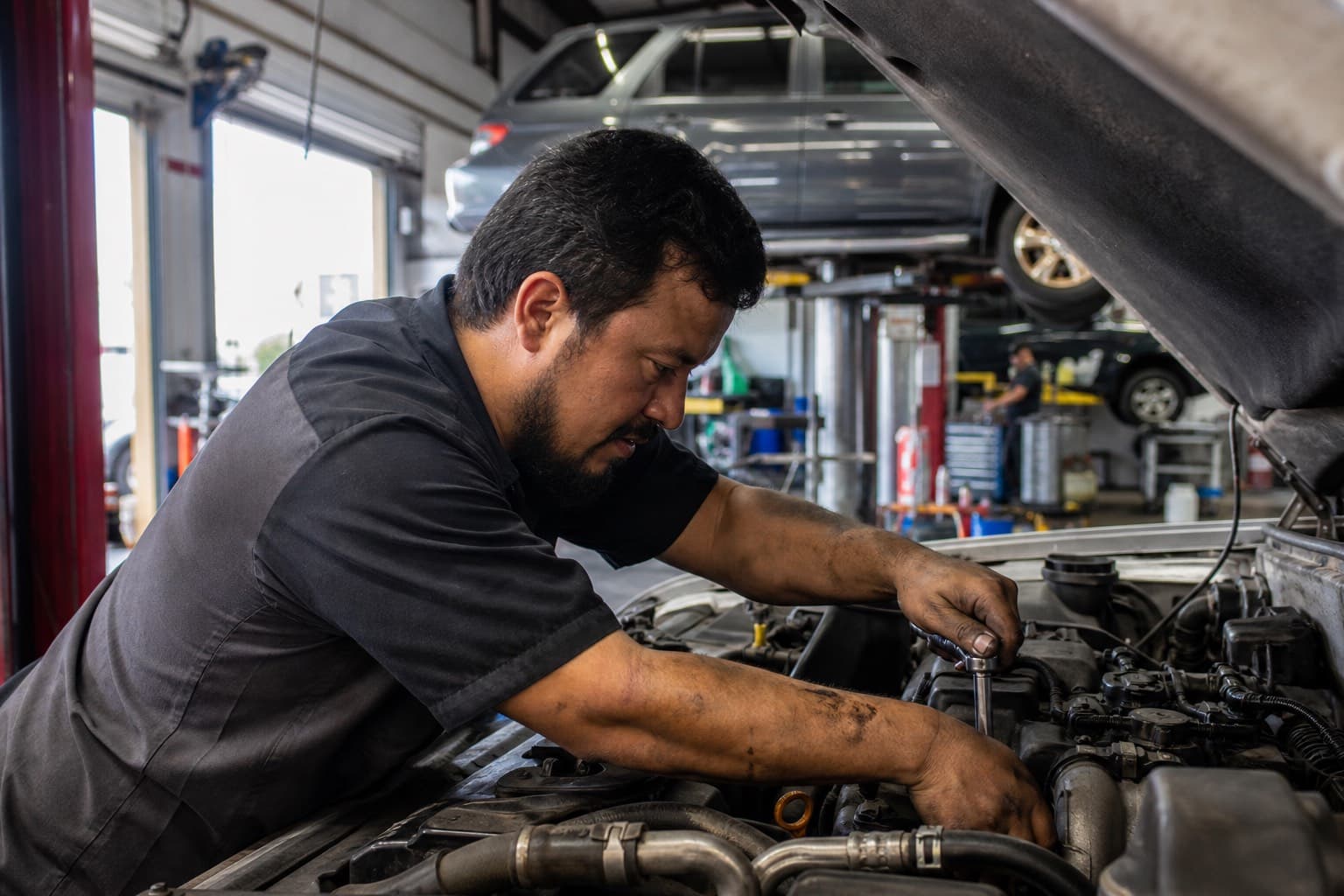 Mechanic working under the hood of a car in a busy shop